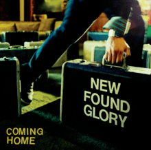 A photo of lead vocalist Jordan Pundik walking out of a restaurant holding a suitcase that reads the words &#039;NEW FOUND GLORY'. The words 'COMING HOME' appear in the bottom-left of the image.